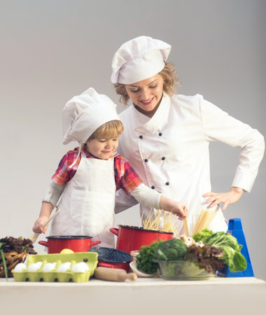 Mother and baby cooking in kitchen. Kid baby helping mom in kitchen. Mother and son cooking healthy meal in kitchen. Baby chef with Mother with apron on kitchen. Cooking at home. Child chef.の写真素材