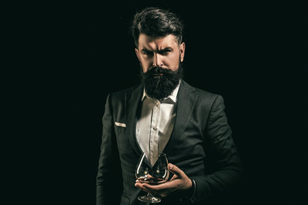 Whiskey glass held by bearded man. Guy drinking whiskey alone at bar. Whiskey pour in classic vintage glass. Whiskey tasting with retro style. Expensive whisky. Cognac or whisky. Alcoholic beverage.の写真素材