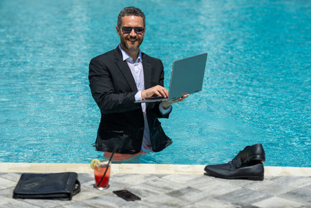 Funny business. Remote job by beach. Summer vacation with laptop. Freelance summer business. Business humor. Handsome businessman in suit swim in water. Relaxing after job. Success and crazy business.の写真素材