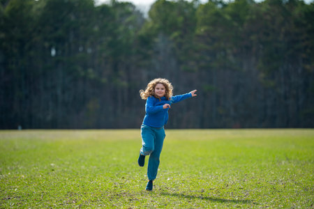 Child running on field. Happy kid running outdoors. Child jumping and running in nature. Child running in a meadow. Summer fun for active child. Playful kid freedom. Free childhood in nature.の写真素材
