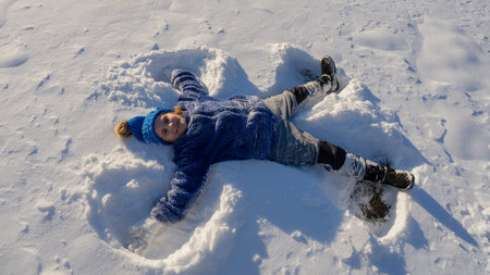 Child making a snow angel. Happy kid lying in the snow. Kid angel in snow. Winter kids with snowy...