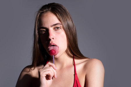 Lollypop in woman mouth. Girl enjoys sweets. Model licks a candy treat. Beautiful woman with a...