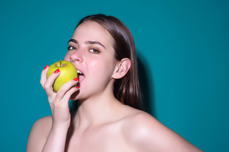 Young happy smiling woman bitting apple, healthy lifestyle. Girls holds a fresh green apple studio portrait on isolated background. Healthy food. Fruit for healthy teeth. Woman holding apple.の写真素材