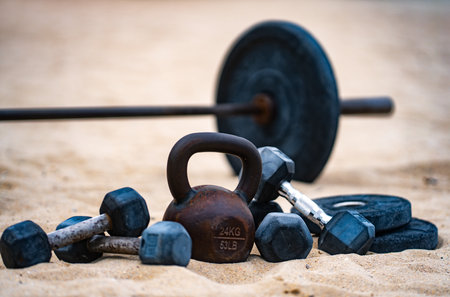 Outdoor gym background. Metal kettlebell on sand. Urban gum in outdoor gym. Natural workout. Gym weights background. Summer training background. Barbell and dumbbell background.の写真素材