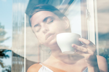 Romantic woman drinking espresso. Attractive brunette holding coffee cup. Girl enjoying aromatic latte. Romantic portrait of woman with coffee in cafeteria. Model with coffee glass. Delicious coffee.の写真素材