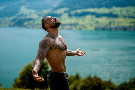 Carefree man in nature. Man in alpine landscape. Muscular guy breathing fresh air. Handsome topless model with raised hands. Peaceful hispanic man meditating. Sexy man in meditation pose.の写真素材