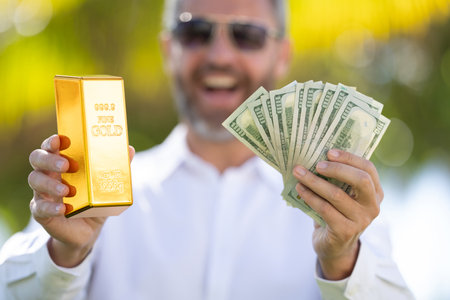 Business man holding a gold bar and cash. Gold financial success. Successful rich man holding gold...