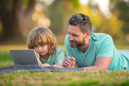 Family, leisure and people concept. Happy father and son with tablet pc computer laying on grass. Kid with daddy learning online lesson.の写真素材