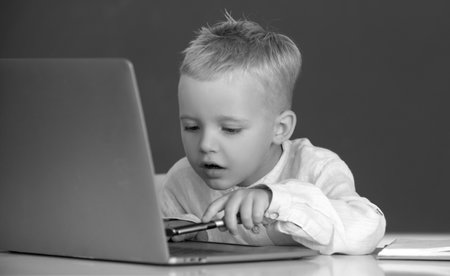 School child using digital pc laptop in class. Portrait of funny pupil of primary school study programming. Funny blonde pupil on blackboard.の写真素材