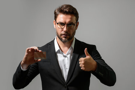 Business man holding a credit card on gray isolated background. Hispanic man showing credit card. Credit or deposit bank card. Online shopping concept. Offer discount sale, online shopping.の写真素材