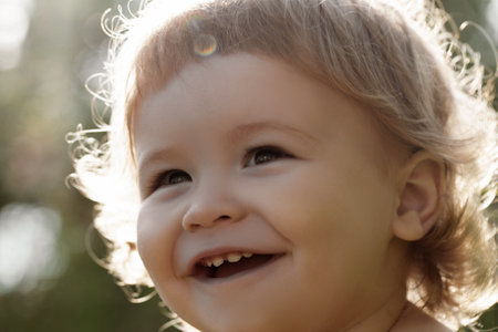 Close up portrait of a small blond baby boy. Funny kids cropped face outdoor on sunny day. Kids smiling, cute smile.の写真素材