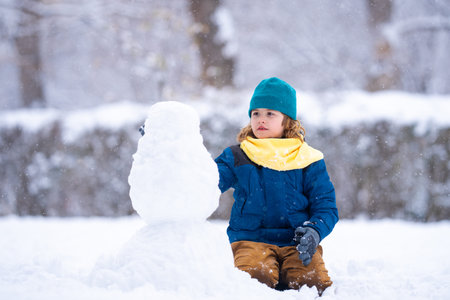 Kid play with snowman in winter. Snowman with a carrot nose on a winters day. Child making snowman. Little boy building snowmans in snowy park. Child embracing snowman in a snowy winter park.の写真素材