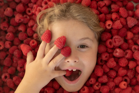 Kid eating raspberries. Close-up portrait of child isolated over raspberry violet purple background.