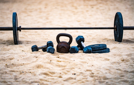 Natural workout. Gym weights in park. Summer training. Barbell and dumbbell set. Exercise outdoors in nature. Kettlebell with heavy weights. Park workout with dumbbells. Weightlifting on the beach.の写真素材
