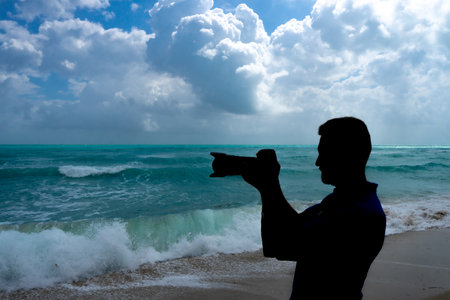Man photographer with a camera on vacation. Summer photographer by the ocean. Tropical travel photography. Photograph of a man by the sea. Photographer capturing tropical views. Tourist photographer.の写真素材