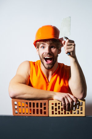 Crazy builder with bricks, funny sale on construction site. Funny man with helmet doing brick work. Builder posing with bricks blocks. Bricklayer concept. Funky handyman. Man in hardhat holding brick.の写真素材