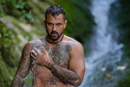 Sexy male body. Shirtless man splashing under waterfall. Fit and strong body. Hispanic man enjoying...