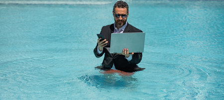 Funny freelancer, distance online work, e-working. Summer funny business. Business man in suit remote working on laptop in water pool. Business man working online on laptop in summer pool.の写真素材