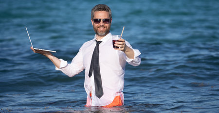 Fun business lifestyle. Freelance work, distance online work, e-working. Summer business. Business man in shirt remote working on laptop in sea water. Business man working online.の写真素材