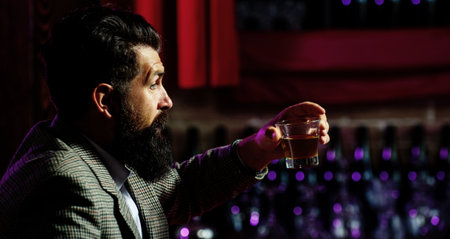 Man drinking whiskey at bar. Handsome man enjoying a drink. Whiskey moment with serious face. Man holding classic whiskey glass. Man tasting aged whiskey alone.の写真素材