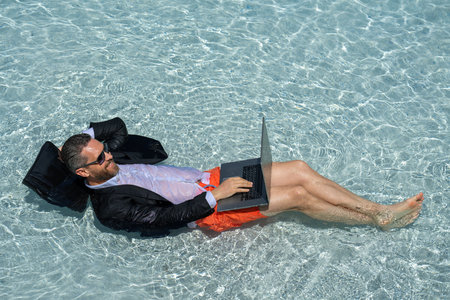 Eastern businessman taking a break. Tropical career escape. Stylish millennial enjoying success. Online work in pool. Wealthy tourist relaxing. Hot summer holiday retreat. Motivated freelancer.の写真素材