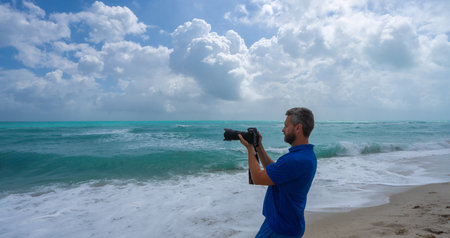 Mature man photographer. Man photographer with a camera on vacation. Traveler photographer by the ocean. Tropical travel photography. Photograph of a man by sea. Photographer capturing tropical ocean.の写真素材
