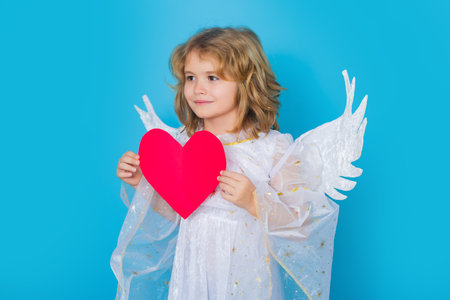 Angel kid with heart. Valentine angel. Little cupid child. Kid angel with angels wings, isolated on blue studio background. Valentines day gift card.の写真素材