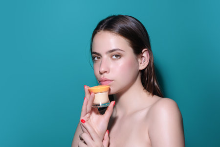 Closeup young woman applying cream to face. Skincare and cosmetics concept. Skin care. Girl applying cream on face on studio background. Skin moisturizer.の写真素材