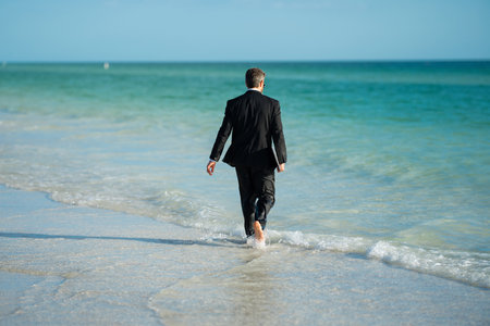 Leisure weekend and remote freelance work. Rear view of back business man in suit in sea water at beach. Remote summer business. Summer holiday.の写真素材