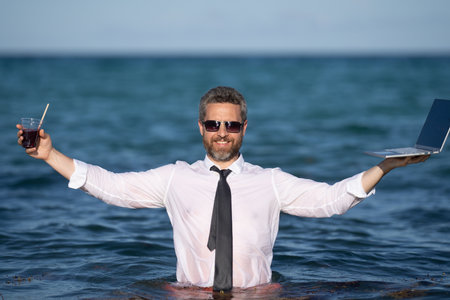Remote online working on summer sea beach. Business man with laptop during tropical beach vacation. Leisure weekend and remote freelance work. Crazy comic businessman rest on sea beach.の写真素材