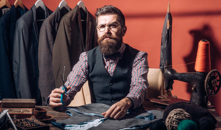 Tailor in his workshop. Suit tailoring. Handsome man is classic tailor. Tailor measuring fabric in a...