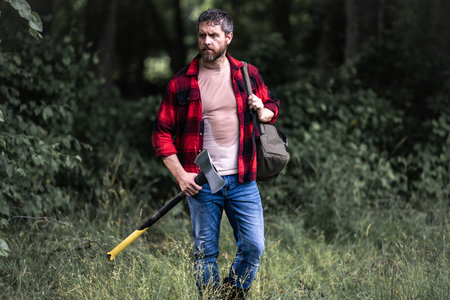 Confident lumberjack works in summer forest. Man with an ax. Woodcutter in plaid shirt in forest. Hipster with axe. Lumberjack with an axe. Bearded lumberjack. American lumberjack with hatchet.の写真素材
