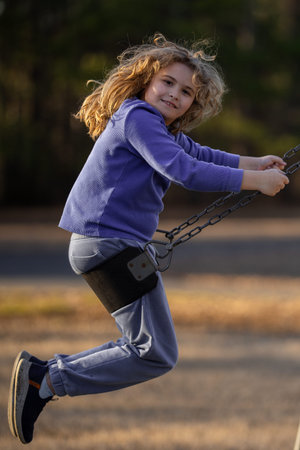 Blonde kid swinging outdoors. Laughing child on swing. Cute kid boy playing at playground. Excited kid on a swing in motion. Cute kid in summer park. Playful child swinging in park. Happy childhood.の写真素材