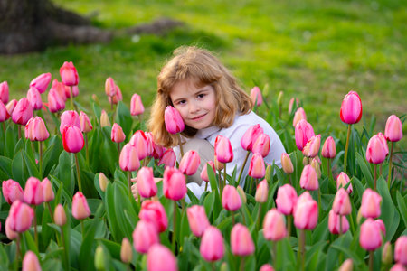 Kid enjoying spring day in tulip field. Child in tulip garden. Little girl playing in blooming tulip meadow on spring day. Spring kids face. Child smelling tulip in spring park. Children concept.の写真素材