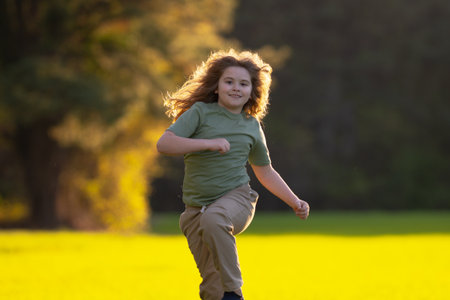 Child running in summer field. Happy kid run outdoors. Child on nature. Child in run motion on grass. Kid running at sun light. Teen running in meadow. Portrait of running child.の写真素材
