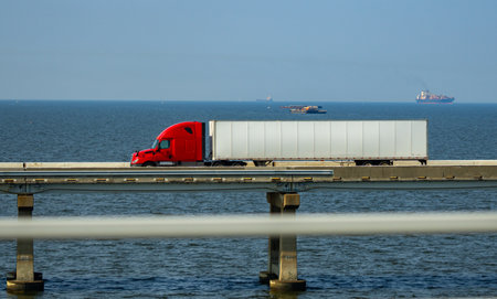 Truck driving across the bridge near sea or ocean. Lorry transporting. Cargo trailer. Logistics truck, international shipment. Heavy-duty truck transport. Semi truck containers, logistics industry.の写真素材