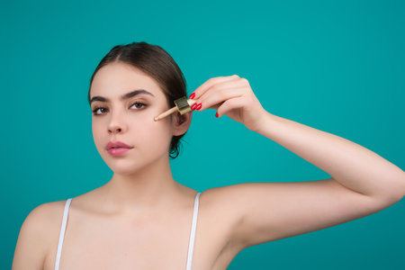 Smiling girl with flawless skin applying treatment cream isoalated on studio background. Skin care concept. Mockup dropper lid in female hands. Cosmetic product, serum. Concept of beauty.の写真素材
