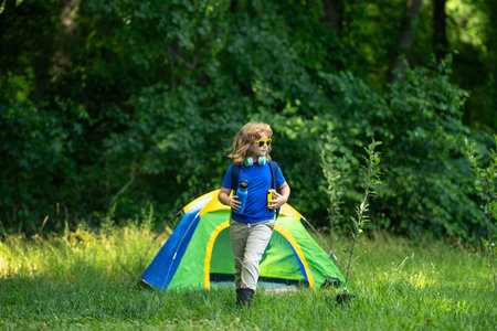 Kid exploring nature outdoors. Child hiking in the forest. Kid on camping. Kid with backpack on a nature trail. Little traveler. Child tourist near a tent outdoor. Little explorer with camping gear.の写真素材