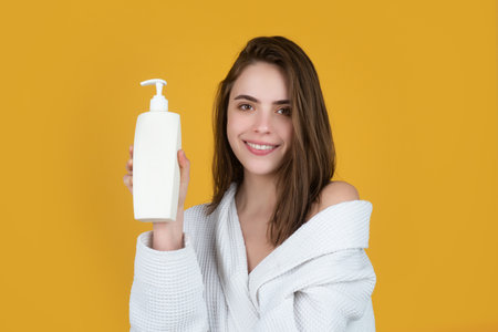 Beauty portrait. A beautiful girl with clean skin holds a template tube in her hands. Women hair care, bottle shampoo and conditioner, beauty product. Brunette girl with haircare shampoo.の写真素材