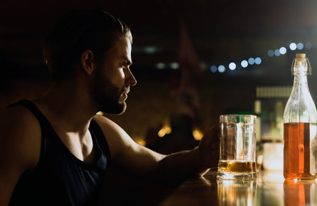 Alcohol addiction. Sad man in dark bar. Alcohol problem. Lonely man drinking at restaurant. Drinking alcohol. Depressed man with glass of alcohol. Hopeless alcoholic facing responsibility.の写真素材