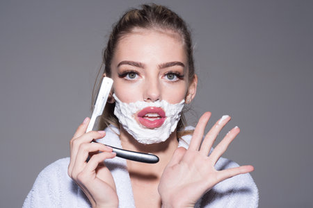 Woman shaving face with gentle foam. Girl removing facial hair. Razor and skincare cream for facial hair. Young woman applying shaving cream on upper lip. Comic hair removal. Concept of facial hair.の写真素材