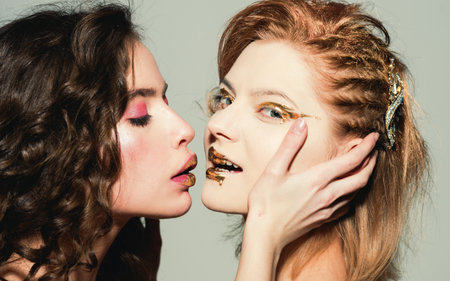 Woman kissing with art makeup. Sexy portrait of two beautiful women in colorful makeup. Closeup of female faces painted with vibrant cosmetics. Sexy and creative makeup art. Facial art makeup.の写真素材