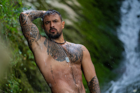 Shirtless man splashing under waterfall. Fit and strong body. Strong man enjoying summer water. Athletic male body. Man beauty on nature. Muscular body with water drops.の写真素材