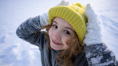 Child play in snowy park. Kid plays in falling snowflakes. Winter fun. Portrait of kid in winter....