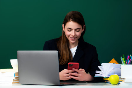 Female student using phone in classroom. School girl chatting on mobile phone near blackboard....