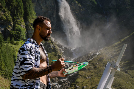 Artist hipster man drawing outdoor. Painting art. Man artist draw pictures in alps mountain. Man painting with brushes oil or acrylic paint. Male artist paints a picture on canvas.の写真素材