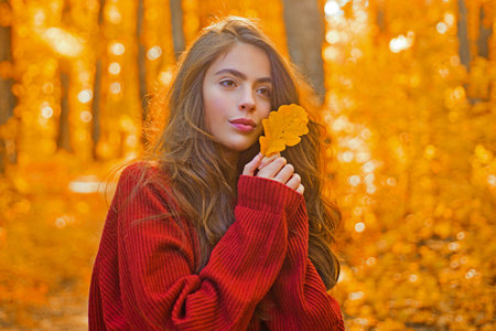 Portrait of woman with autumn leaf on face. Woman portrait close up on autumn background. Woman face...