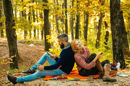 Couple on picnic. Family camp on autumn nature. Couple on picnic in autumn forest. Couple in Autumn fall park. Man and woman near Autumn fall leaves.の写真素材