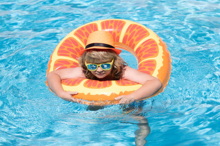 Child in swimming pool on inflatable ring. Kid swim with orange float. Water toy, healthy outdoor...