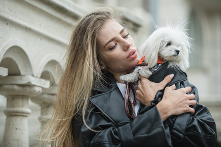 Woman hugging fluffy puppy outdoors. Girl playing with cute bolognese dog. Young woman holding small white dog. Fluffy puppy. Girl cuddling her domestic doggy. Smiling woman with cute dog outdoor.の写真素材